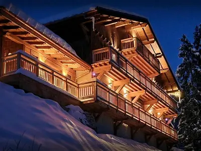 a house with a deck in the snow at night at Chalet Les Pellys - OVO Network in Samoëns