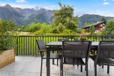 a patio with a table and chairs and mountains at La Yaute Chamonix-Les Houches in Les Houches