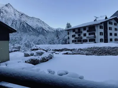 a building covered in snow with mountains in the background at Capucins 3 in Chamonix-Mont-Blanc