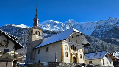 a church with a clock tower with mountains in the background at Appartement proche télécabine! Séjour tout inclu! in Les Contamines-Montjoie