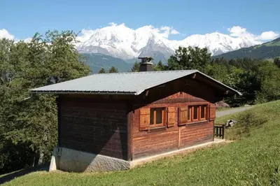 a small cabin on a hill with mountains in the background at Charmant petit chalet cosy in Combloux