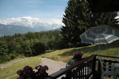 a bench with an umbrella on a balcony with mountains at Charmant petit chalet cosy in Combloux