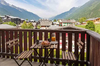 a table with a bowl of food on a balcony with mountains at Les Trois Balcons Apartment - Chamonix All Year in Chamonix-Mont-Blanc