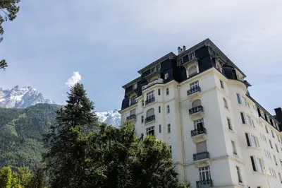 a tall white building with mountains in the background at Le Majestic 145 Apartment - Chamonix All Year in Chamonix-Mont-Blanc
