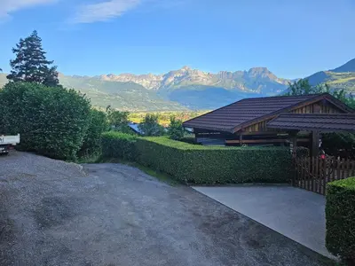 a house with a fence and a building with mountains in the background at Apartment in Saint-Gervais close to gondola in Saint-Gervais-les-Bains