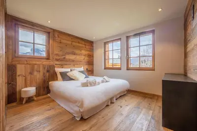 a bedroom with a large bed with wooden floors and windows at Chalet Les Marmottes in Combloux