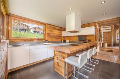 a kitchen with white cabinets and a wooden wall at Chalet Les Marmottes in Combloux