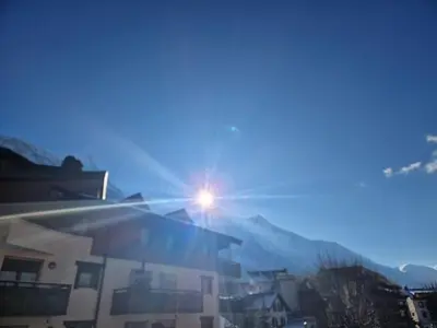 a sun shining on a building with mountains in the background at La Ginabelle 2 - Vue MontBlanc in Chamonix-Mont-Blanc