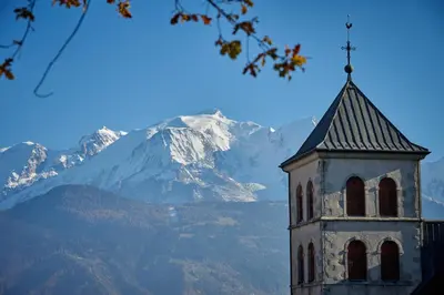 a clock tower with a mountain in the background at Le Miroir De Saint-Jacques in Sallanches