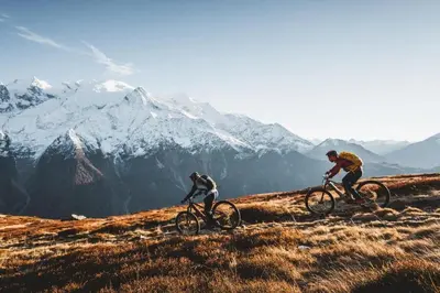two people riding bikes on a hill with mountains in the background at Au Coin du Mont Blanc in Chamonix-Mont-Blanc