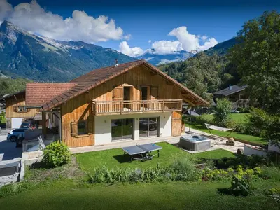 a house with a porch and a deck with mountains in the background at Chalet Nordchamp - OVO Network in Samoëns