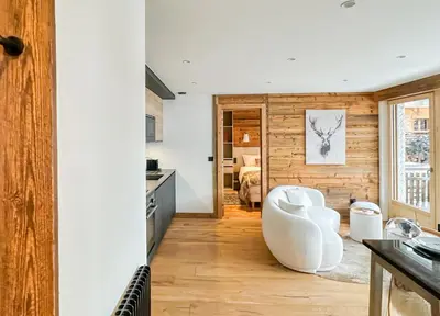 a living room with a white chair and a kitchen at My Way Megeve village 5 rues parking in Megève
