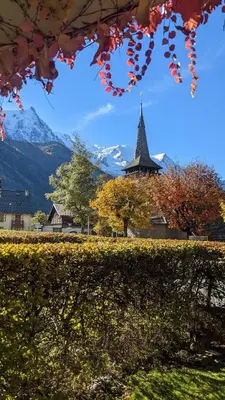 a church with a steeple in the background with trees and leaves at Bright, warm 2BR 2min to gondola, private garden in Chamonix-Mont-Blanc