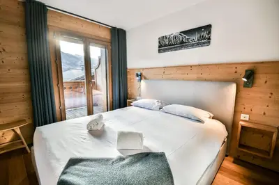 a bedroom with a large white bed with a window at Les Carlines 01 in Samoëns