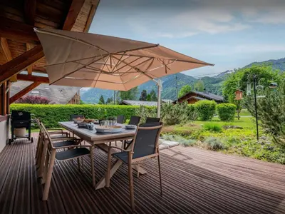 a table with chairs and an umbrella on a deck at Chalet OCimes - OVO Network in Samoëns