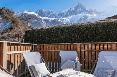 a table and chairs on a fence with snow covered mountains at Duplex T3 with terrace in Chamonix in Chamonix-Mont-Blanc