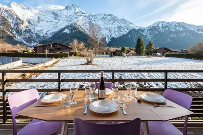 a table with a bottle of wine on a balcony with mountains at Apartment Annapurna, Alpes Travel, Les Houches, Sleeps 5 in Les Houches