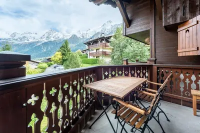 a table and chairs on a balcony with a view of mountains at Appartement aux Houches Pied des pistes in Les Houches