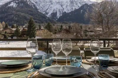 a table with wine glasses and plates on a table with mountains at Nid d'Aigle - Balcon avec vue Mont Blanc in Les Houches