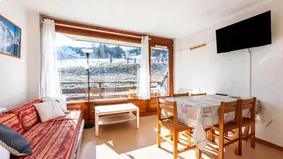 a living room with a table and a couch and a window at Les Eterlous N07 - 2P5 in Morillon
