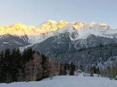 a snow covered mountain range with a house in the foreground at Le Cocon des Cîmes in Les Contamines-Montjoie