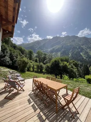 a wooden deck with a table and chairs and mountains at Ferme des Tétras - Chalet de prestige en montagne in Saint-Gervais-les-Bains