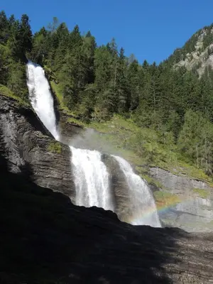 a waterfall on the side of a mountain with a rainbow at Le Samoëns cosy 3 etoiles en centre ville in Samoëns