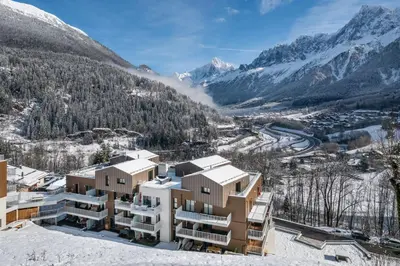 a building in the snow with mountains in the background at Apartment Camox, Les Houches - by EMERALD STAY in Les Houches