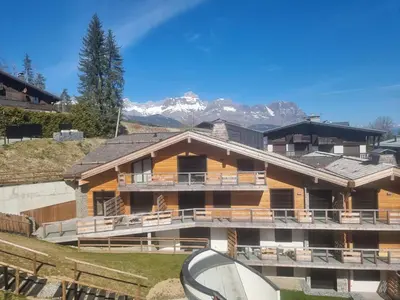 a large building with mountains in the background at Appartement neuf 2 chambres près des pistes à Combloux avec parking - FR-1-560-158 in Combloux
