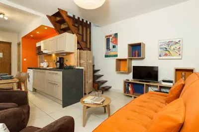 a living room with an orange couch and a kitchen at Apartment Maisonnee - A Charming Chamonix Haven in Chamonix-Mont-Blanc