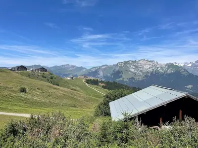 a barn on a hill with mountains in the background at Samoëns 1600 au pied des pistes in Samoëns