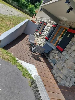 a wooden deck with two chairs and a stone wall at Appartement adapté PMR 4 personnes Saint Gervais les Bains in Saint-Gervais-les-Bains