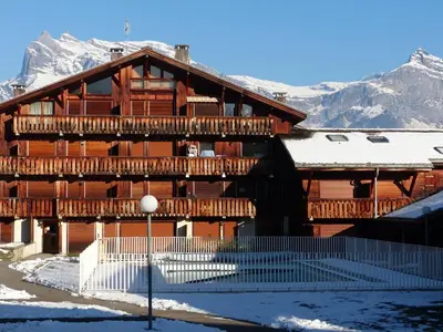a large wooden building with snowy mountains in the background at Cosy alpine apartment with pool and stunning views in Saint-Gervais-les-Bains