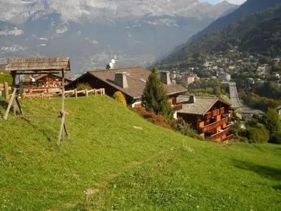 a house on top of a green hill at Cosy alpine apartment with pool and stunning views in Saint-Gervais-les-Bains