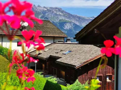 a house with a mountain in the background with pink flowers at Duplex Saint Gervais in Saint-Gervais-les-Bains