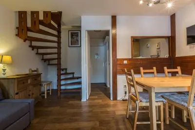 a living room with a dining room table and a staircase at Apartment Jonquille 3 - A Comfortable Chamonix Haven in Chamonix-Mont-Blanc
