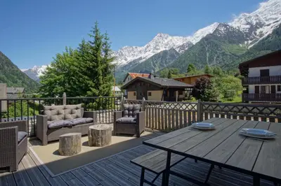 a deck with a table and chairs and mountains at La Terrasse- Panoramique- Familial-Près des pistes in Les Houches