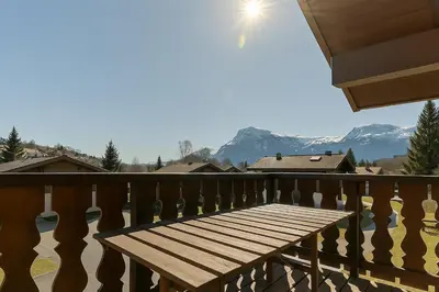 a wooden bench on a balcony with mountains in the background at Appartement avec superbe vue montagne in Arâches-la-Frasse