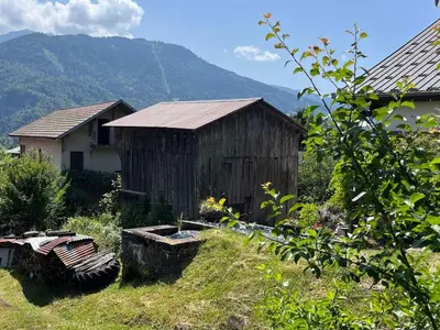 an old wooden shed in a field with a house at Charmant T2 cabine exposé Ouest avec parking couvert - FR-1-629-148 in Samoëns
