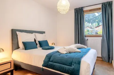 a bedroom with a bed with blue pillows and a window at Appartement moderne - Les houches in Les Houches