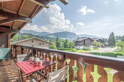 a balcony with a red table and chairs and mountains at Appartement Warens - Welkeys in Megève