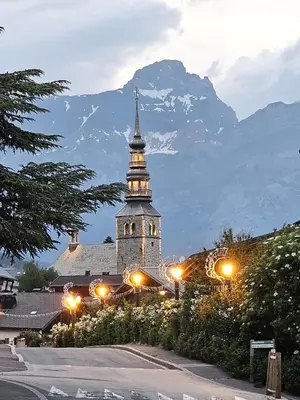 a building with a clock tower in front of a mountain at Chalet Double M I Le Chalet Club in Combloux