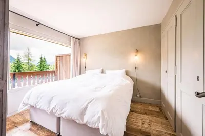 a bedroom with a white bed and a large window at Apartment with balcony 10 min walk from the slopes in Megève