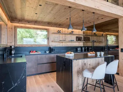 a kitchen with a black counter and white chairs at Chalet Victory I Le Chalet Club in Combloux