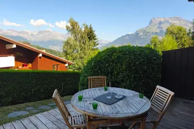 a wooden table and chairs on a patio with mountains at South-facing flat with garden near city center in Saint-Gervais-les-Bains