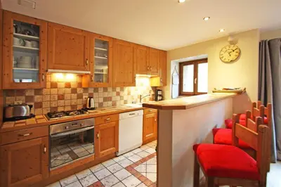 a kitchen with wooden cabinets and a counter with red chairs at La Ferme des Praz apartment - Chamonix All Year in Chamonix-Mont-Blanc