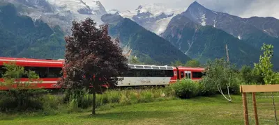a red and white train traveling through the mountains at Grand studio près Lac Gaillands in Chamonix-Mont-Blanc