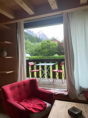a living room with a red chair and a balcony at Appartement exceptionnel au Lavancher à chamonix in Chamonix-Mont-Blanc