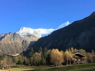 a house in a field with mountains in the background at L'aiguille in Saint-Gervais-les-Bains