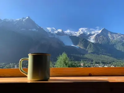 a coffee cup sitting on a window sill with a view of mountains at Amazing Mt Blanc View 2 Bed, Parking, 10mins walk in Chamonix-Mont-Blanc
